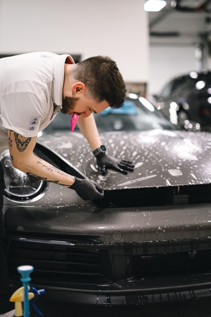 A mechanic carefully working on a black car in a modern auto repair garage.